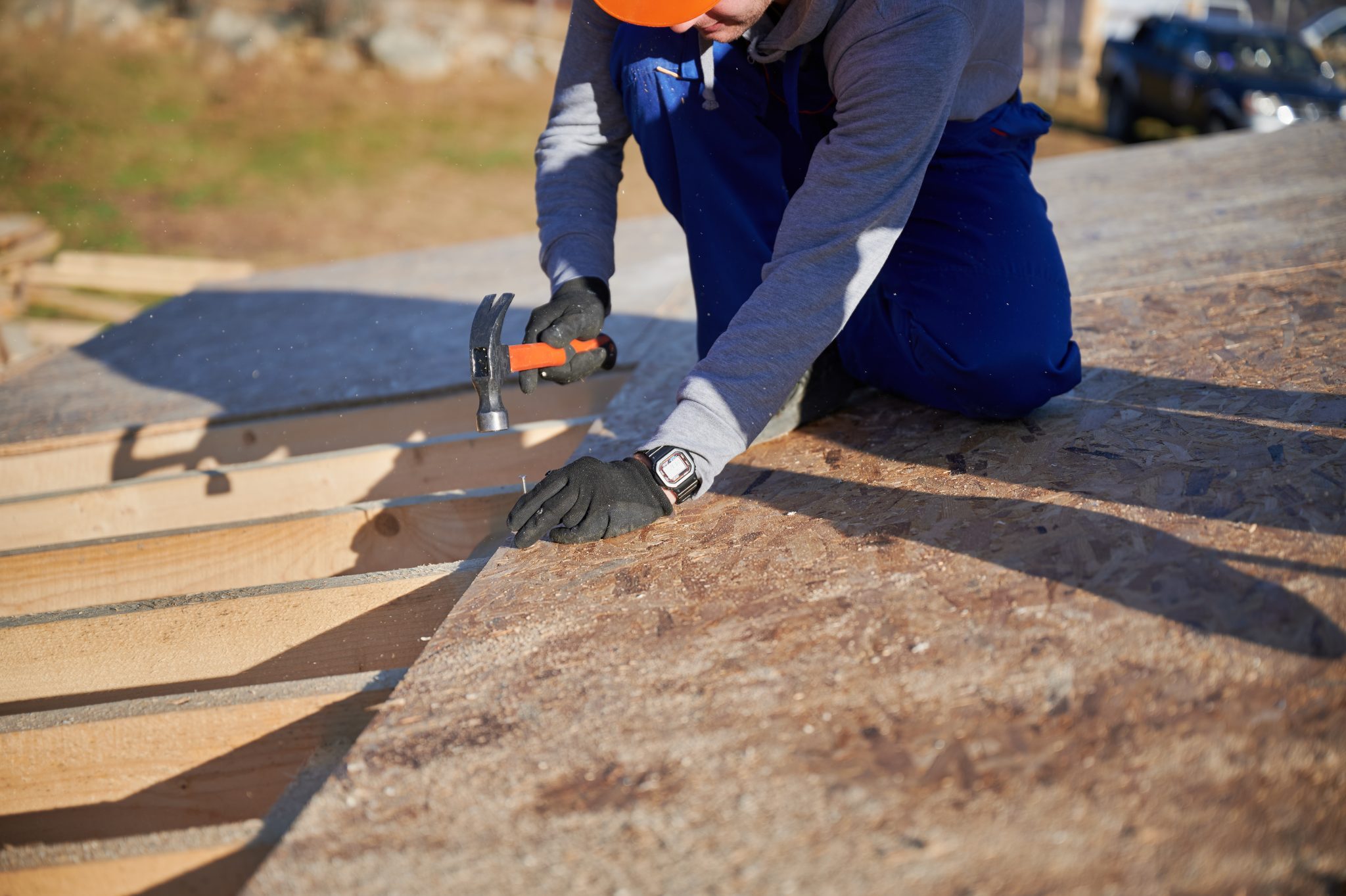 Carpenter hammering nail into OSB panel on the roof top of future cottage. Man worker building wooden frame house. Carpentry and construction concept.